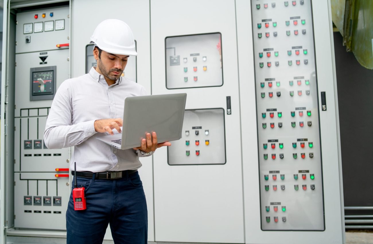 Caucasian engineer man use laptop in front of electrical control panel during process of  maintenance in construction site.